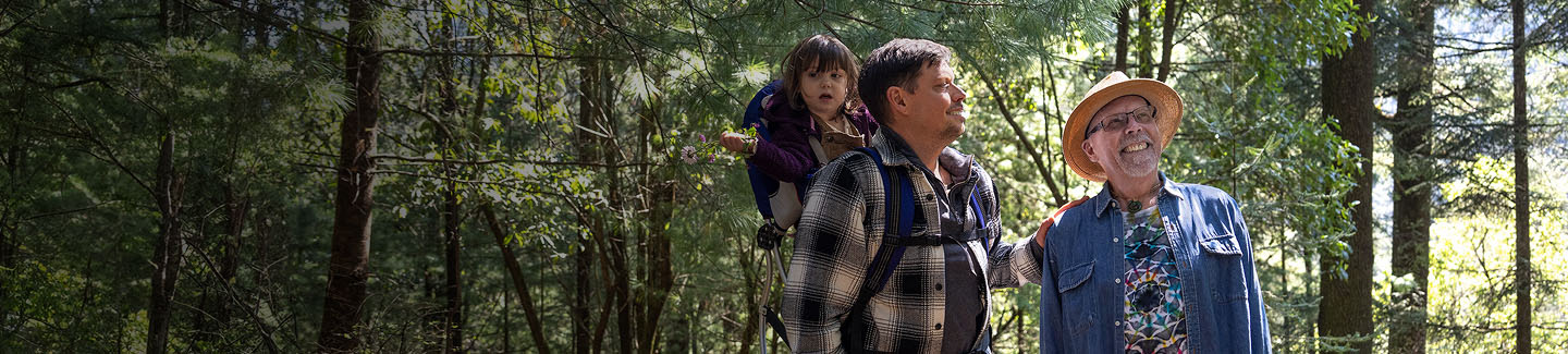 Two men hiking in the woods with a young child in a back harness