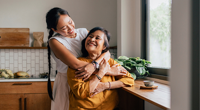 Daughter standing and hugging her sitting mother from behind